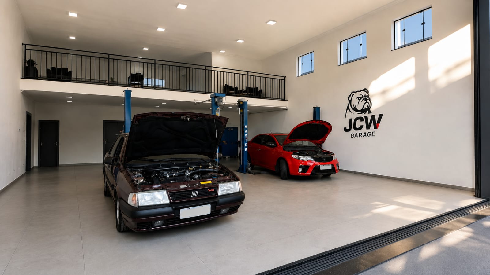 Interior da JCW Garage com veículos sobre elevadores e logo na parede